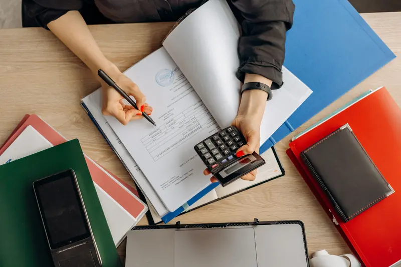 Overhead view of hands reviewing documents with a pen and calculator.
