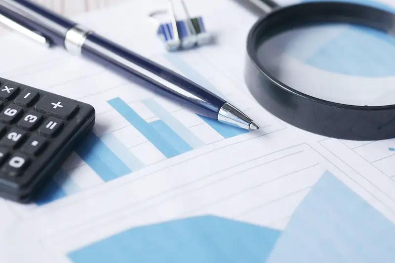 A magnifying glass, pen and calculator resting on printed financial charts.