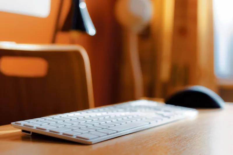 A white computer keyboard and black mouse on a wooden desk.