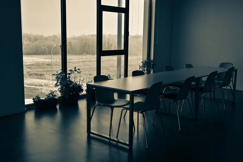 An empty meeting table and chairs beside large windows.